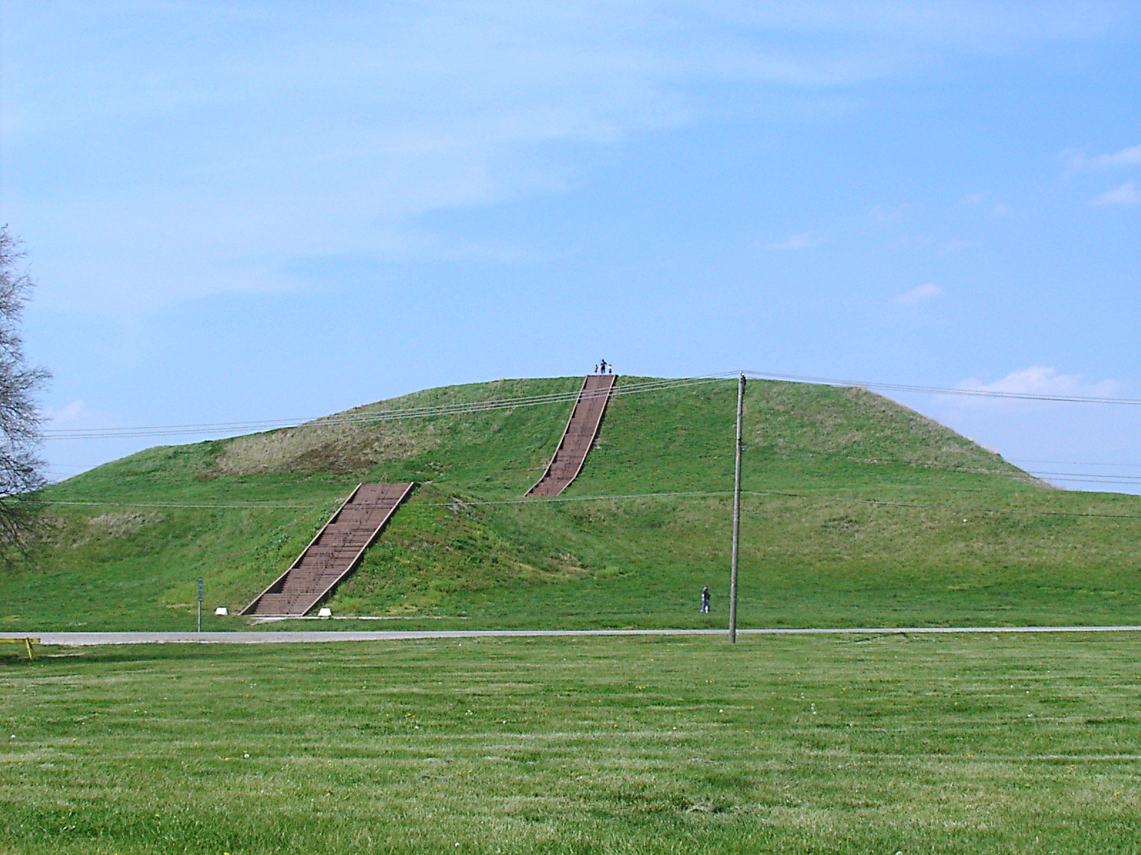 A broad grassy platform mound under open sky, with two wooden staircases