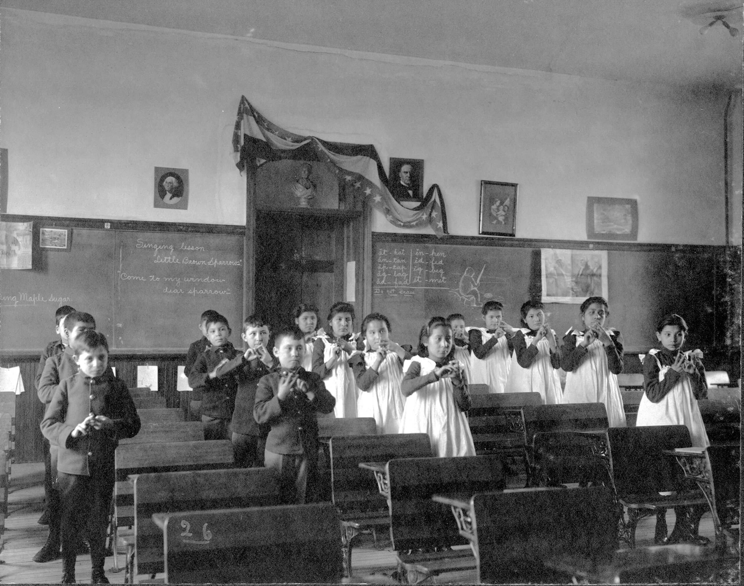 Historical classroom of Native American children in a boarding school, standing in rows for a singing lesson