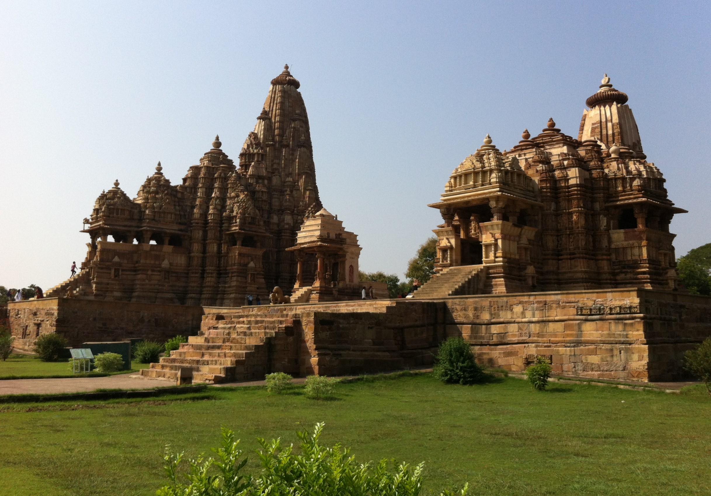 an Indian temple complex with spires and steps, green grass in foreground