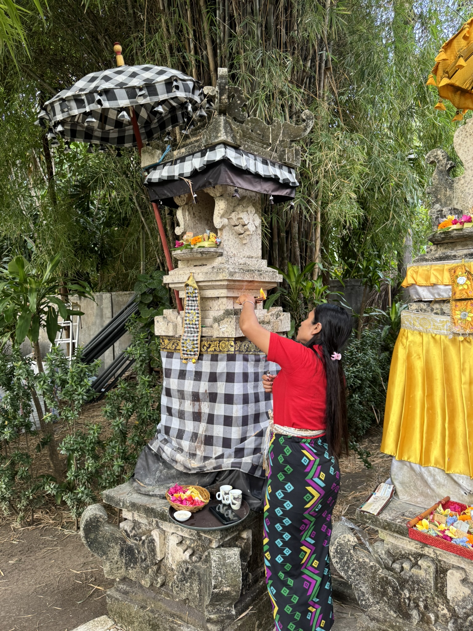a woman with a red shirt makes an offering at a family temple