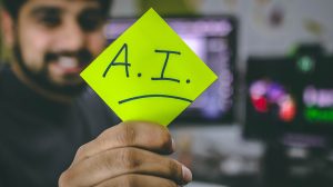 A man holds a post it note that reads "AI."
