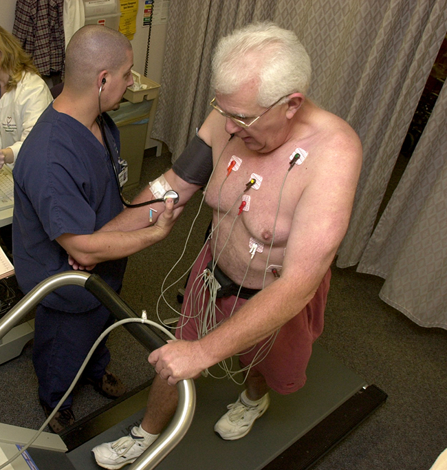 A photo is shown of two men, one walking on a treadmill with various wires connected to his torso region, and the other collecting blood pressure data from the first man.