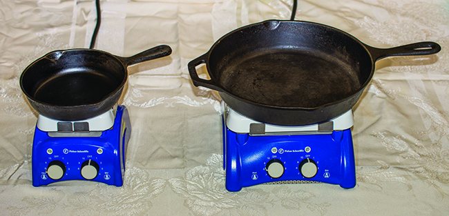 The picture shows two black metal frying pans sitting on a flat surface. The left pan is about half the size of the right pan.