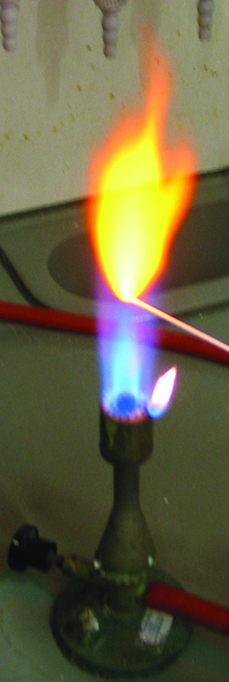 A photo of a lit Bunsen burner is shown. A wooden splint is placed in the flame, and a yellow flame is produced.